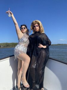 drag queen and bride posing together on bow of a boat